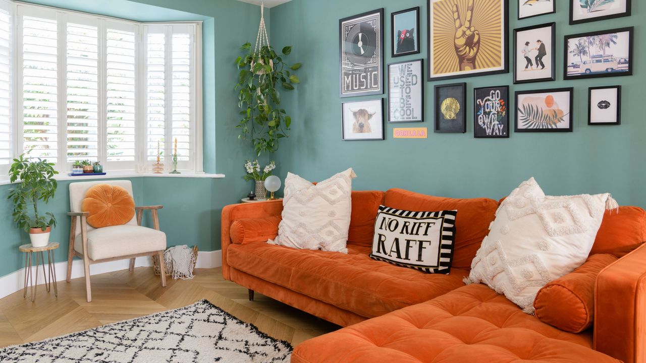 Blue painted living room with a bright orange sofa, a white accent chair, and a large gallery wall behind the sofa