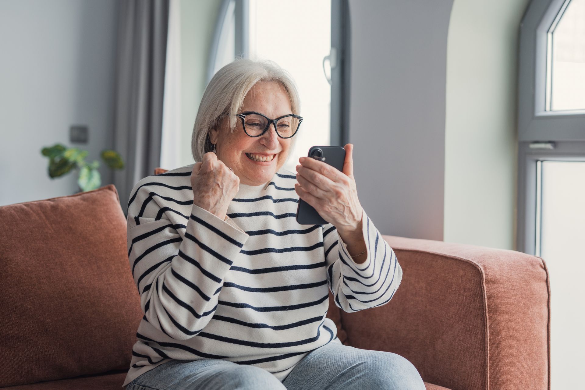 Happy senior woman celebrating success using smartphone
