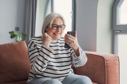 Happy senior woman celebrating success using smartphone