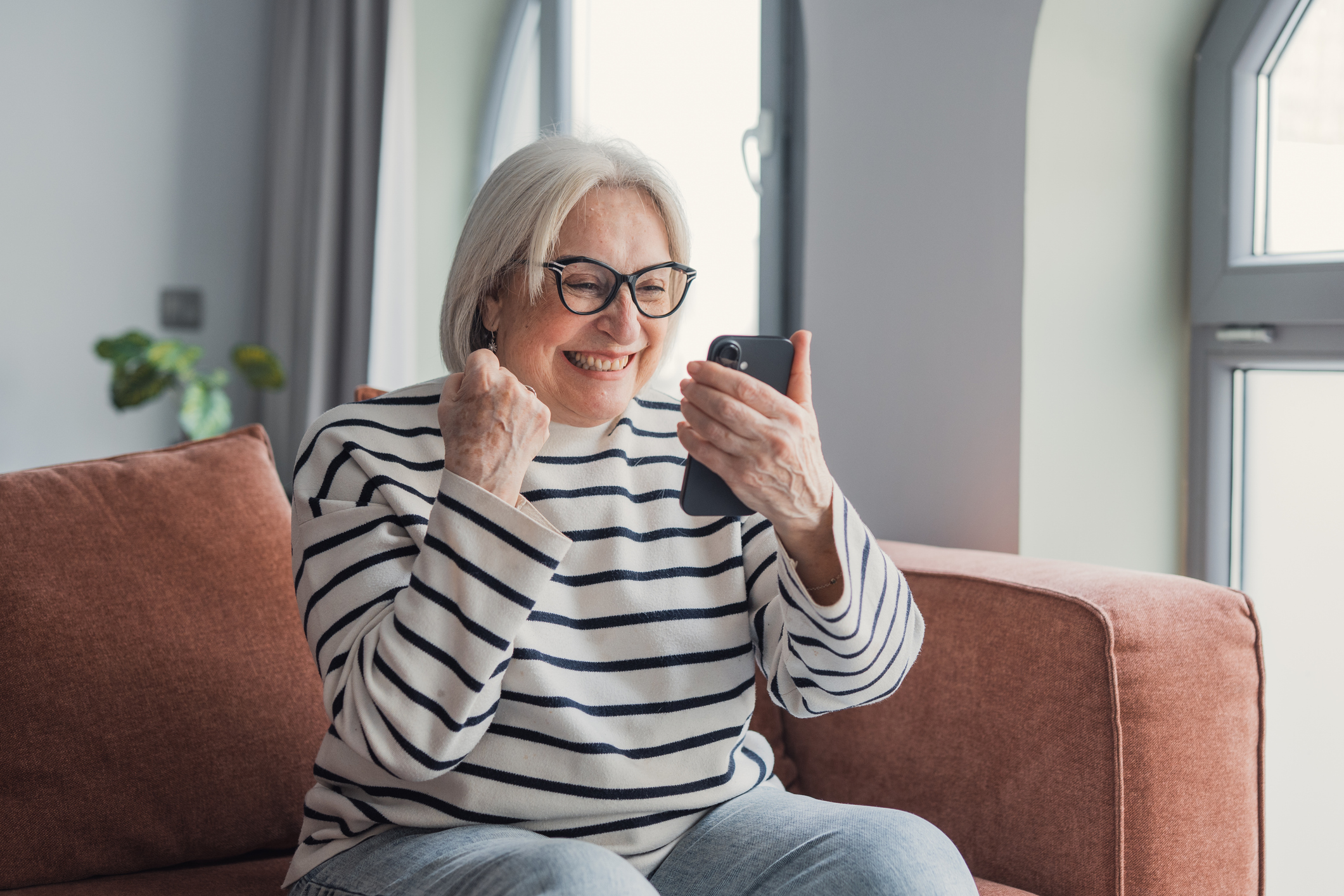 Happy senior woman celebrating success using smartphone