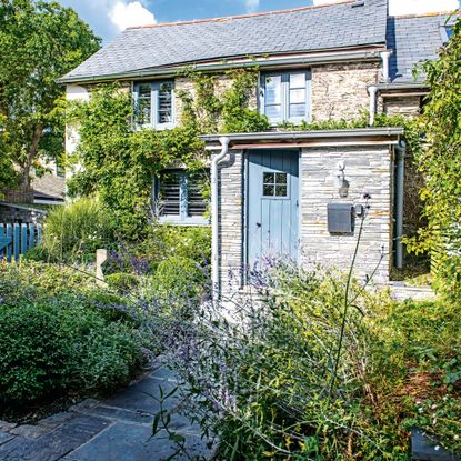 Front of the cottage with paved path, flower beds and blue front door
