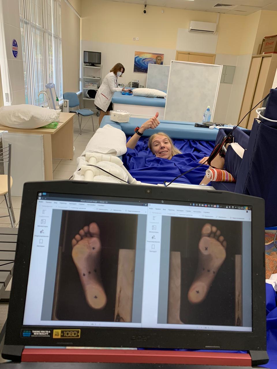 a woman lying on a hospital bed in a laboratory gives a thumbs-up