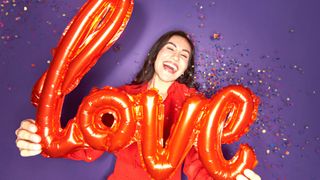 young woman holding love balloon with confetti against purple background