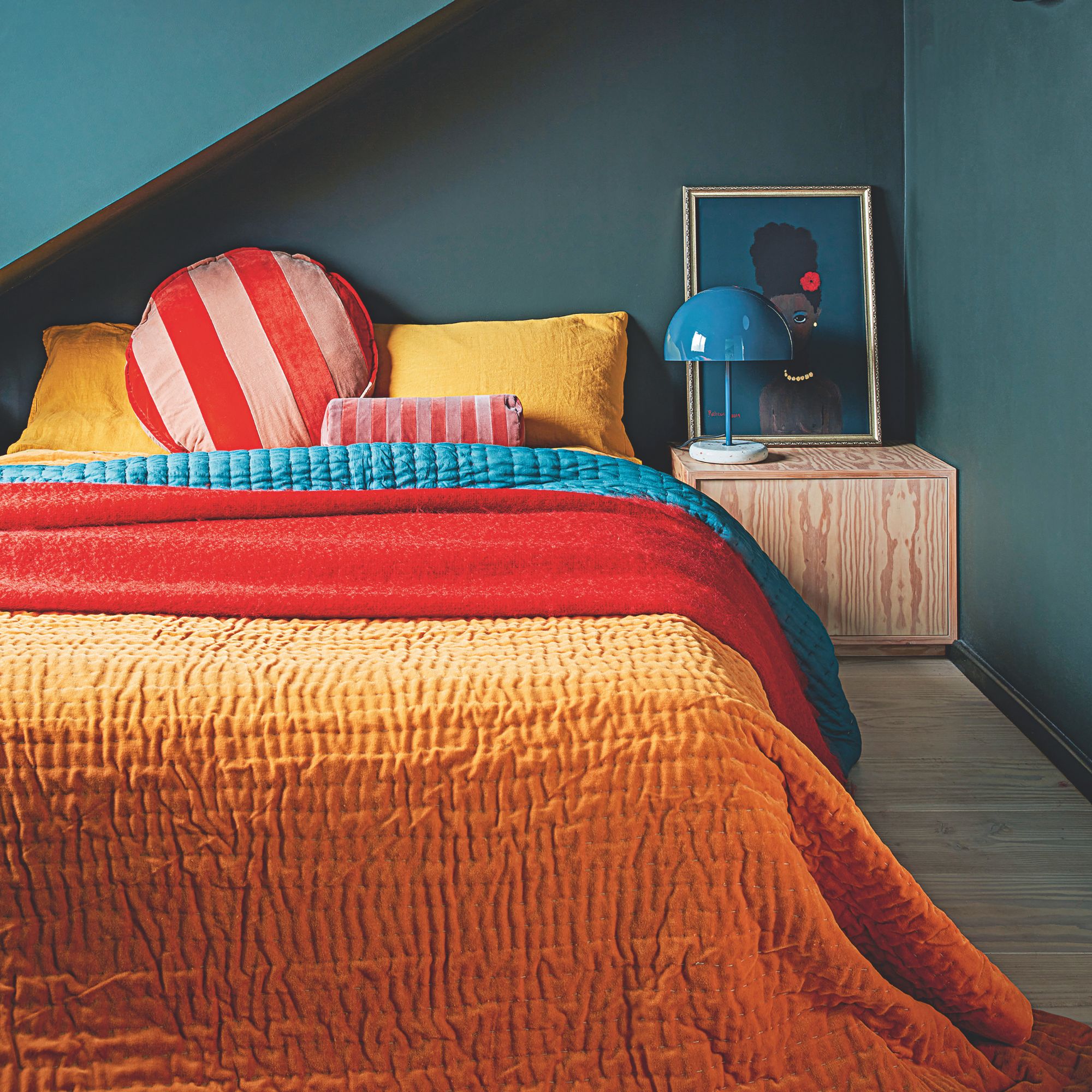 Teal painted bedroom with a bed covered in yellow, red and teal blankets and cushions