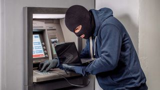 A thief installing a credit card skimmer on an ATM