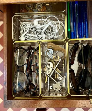 Clear plastic drawer organizers with a gold rim being used to organize small items like keys and sunglasses in a drawer