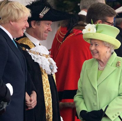 Queen Elizabeth smiling in a green coat while talking to Boris Johnson