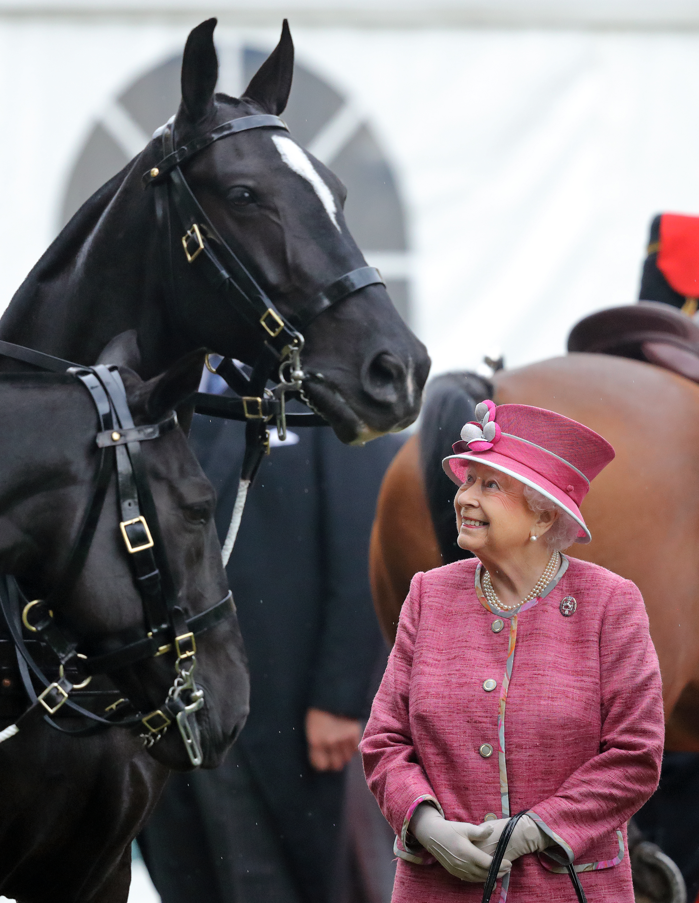Queen Elizabeth wearing a pink coat and hat standing next to two horses