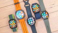 A close-up of five smartwatch on a wooded surface including the Apple Watch SE, Samsung Galaxy Watch Ultra, Google Pixel Watch 3 XL, Apple Watch 10 and Samsung Galaxy Watch 7