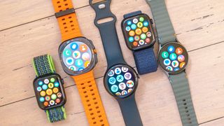 A close-up of five smartwatch on a wooded surface including the Apple Watch SE, Samsung Galaxy Watch Ultra, Google Pixel Watch 3 XL, Apple Watch 10 and Samsung Galaxy Watch 7