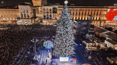 A square in Milan with a tall Christmas tree featuring white lights and crowds of people around