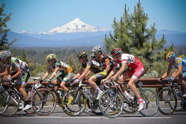 The peloton passes along a road with Bend's mountains in the background.