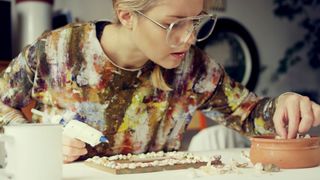 A lady uses a glue gun to attach small shells to a photo frame