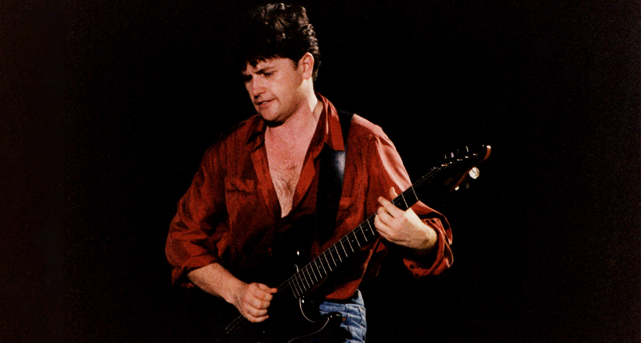 Charlie Burchill of Simple Minds wears a red shirt and plays a Fender Stratocaster onstage in 1989.
