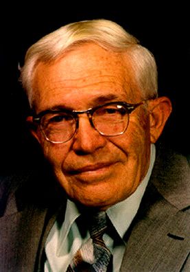 a close up headshot of a man wearing a suit and glasses.