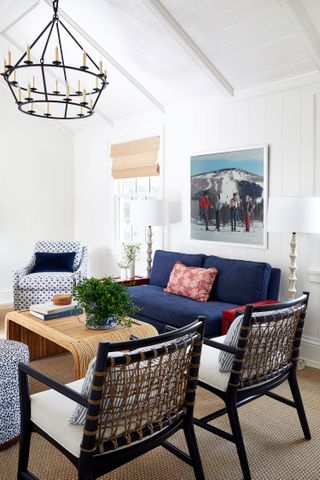 living room with white walls and blue sofa with red cushion and blue patterned armchair wooden coffee table and chandelier above with black bamboo armchairs