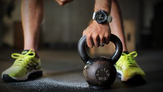 fitness tracker vs running watch: man wearing a running watch lifting a kettlebell