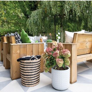 outdoor wooden seating on grey and cream paving slabs, with flowers in a white vase and a woven basket