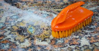Orange scrubbing brush cleaning an outdoor rug