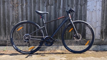 A Scott Sub Cross 50 hybrid bike picture by a wooden fence in a deserted car park