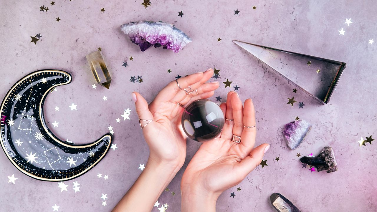  New Year&#039;s resolutions: Hands with rings on fingers are holding crystal ball near esoteric set on concrete gray background with many stars sequins