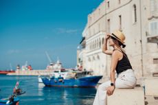 Young Asian woman sitting at the pier in a seaside town in Italy