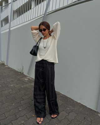 @deborabrosa wearing a cream sweater, Toteme silk pants, black shoulder bag, and Tiffany 
Co. cord bean necklace