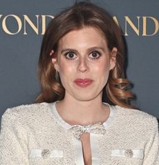 Princess Beatrice wearing a white dress with a cutout featuring bows standing in front of a gray backdrop