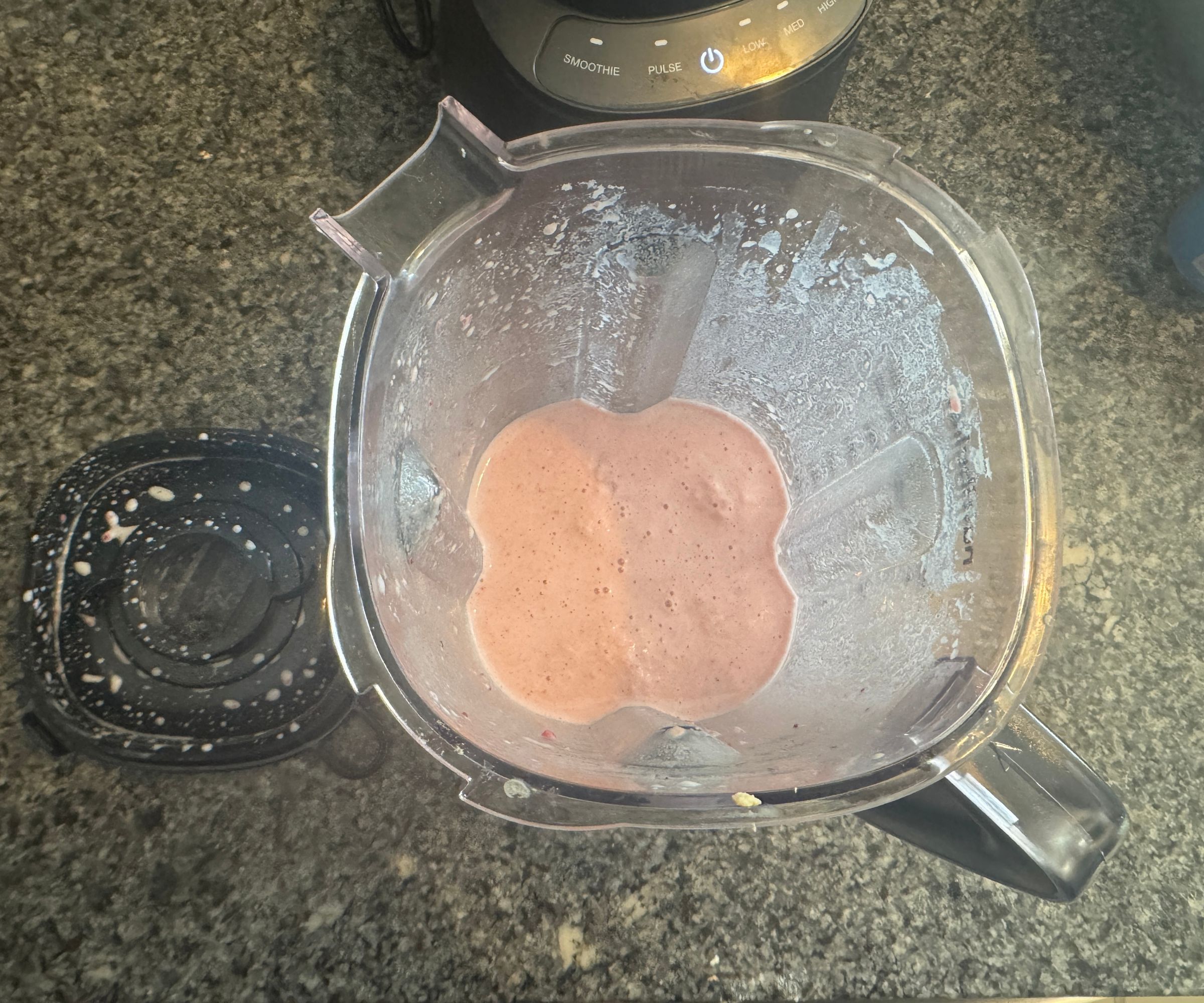 A top down view of a pink smoothie mix inside a clear plastic blender pitcher.