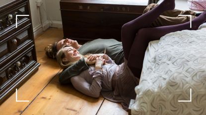 Woman and man lying laughing on the floor together, feet up against bed, representing crazy sex positions