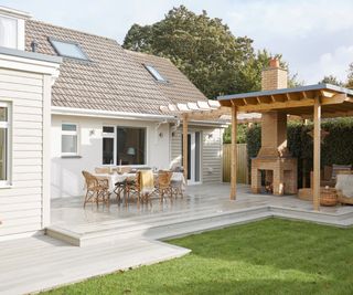 exterior of house with cream cladding, decking area and outdoor fire with chimney