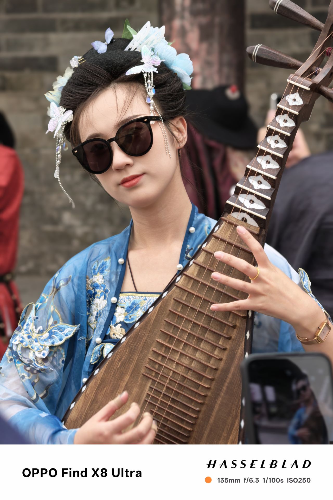 A person in sunglasses and traditional Chinese dress playing an instrument