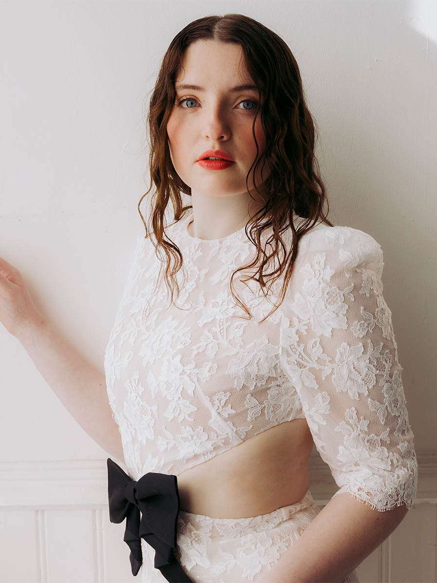 Lucy Halliday photographed by Phill Taylor. She is wearing a white lace dress with center cutout and black bow.