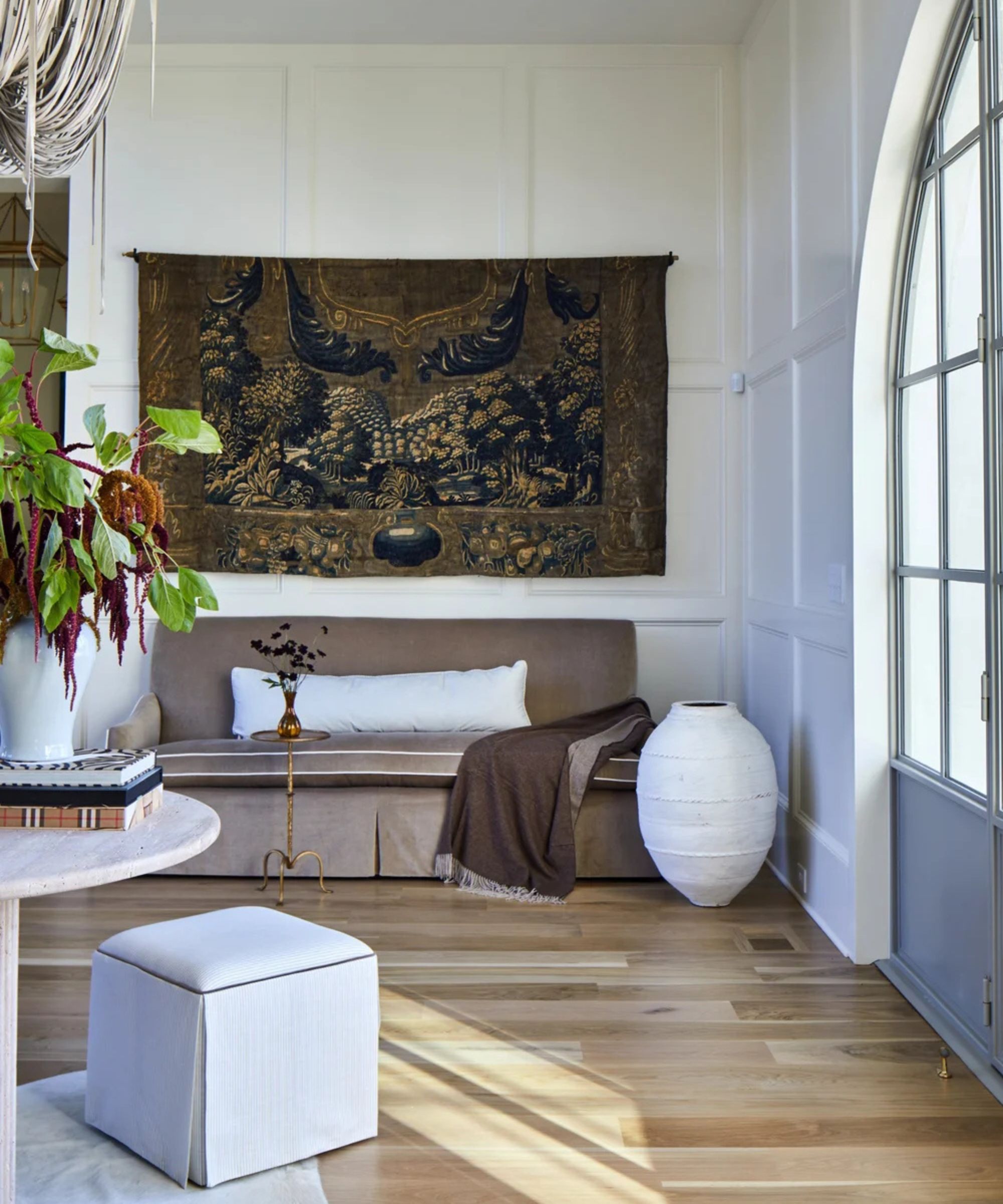 Entryway with white paneled walls and an armless beige couch with a tapestry hanging above