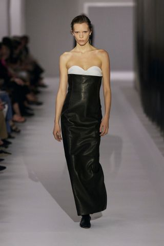 A model wearing a black leather column strapless dress with a white bustier underneath at the S/S 25 Khaite show showcasing the modern socialite trend.