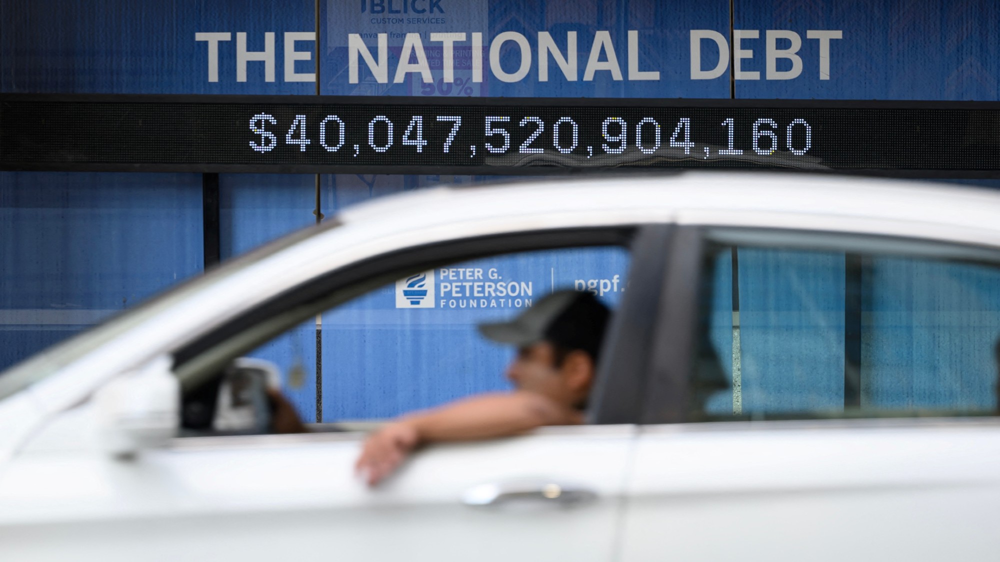 A man drives a car past an electronic tracker showing the national debt amount