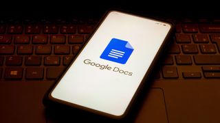 A phone bearing the Google Docs logo sits on a dimly-lit laptop keyboard