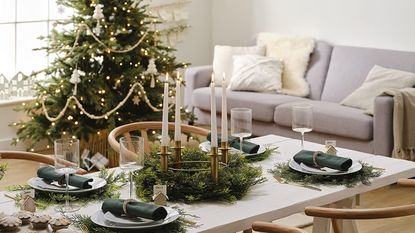 Ginger Ray decorated living room for Christmas with big tree in background, grey sofa, decorated fining table with candles and faux foliage