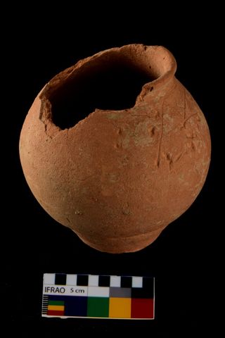 A round, red, chipped pot found in an ancient burial from the indus valley civilization