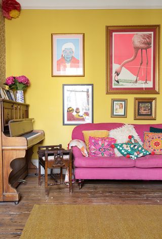 A magenta pink and mustard yellow living room paint color idea with gallery wall, piano and wooden floor and furniture