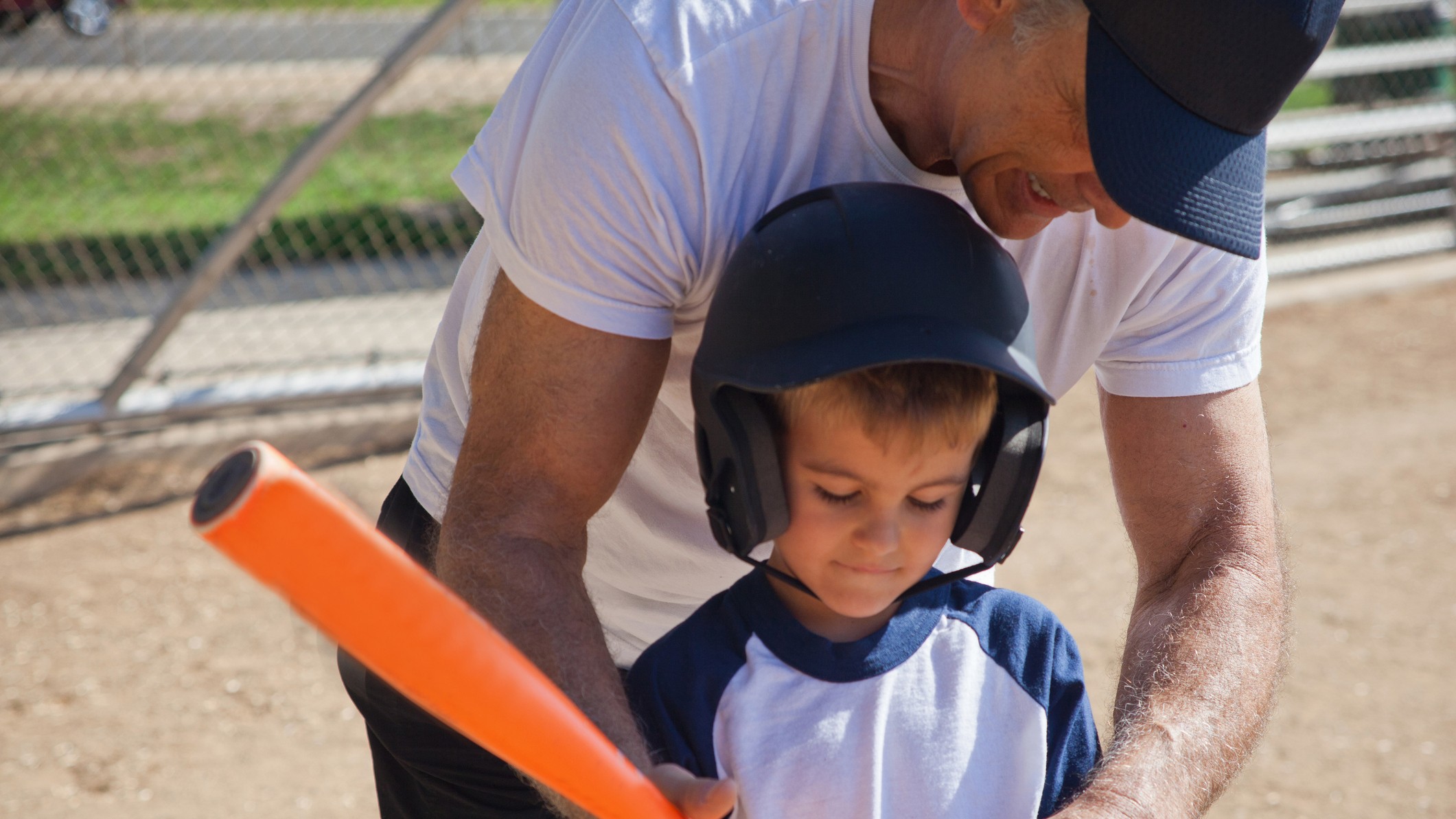 A grandfather is teaching his young grandson how to hit a baseball.