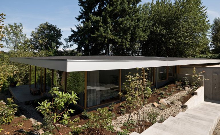 A single-level hillside house, with all glass walls and a flat roof.