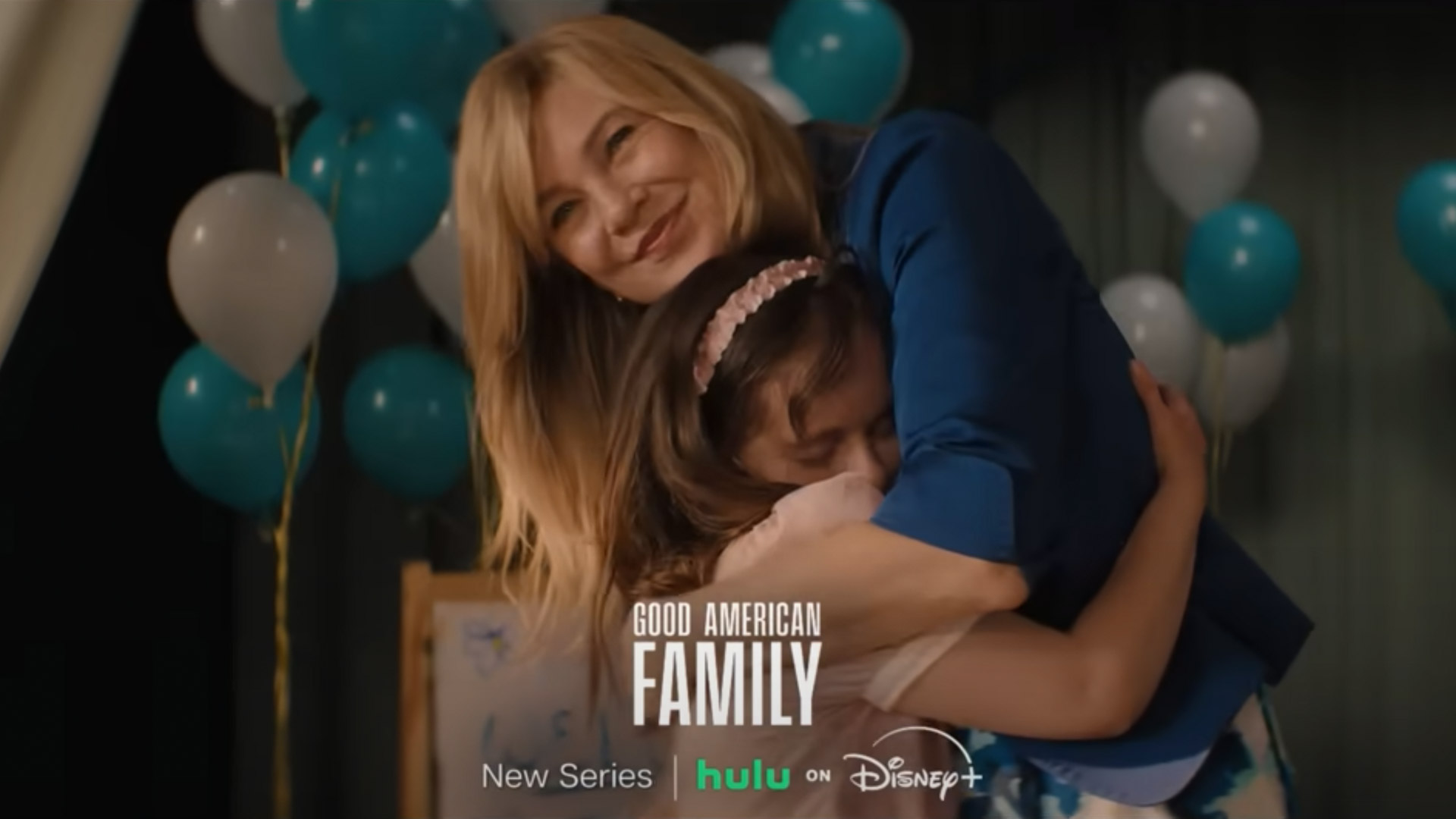 A woman hugs a young girl with balloons in the background