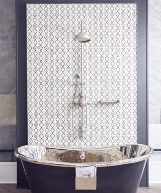 A bathroom with a standalone metal tub and shower head with a tall tiled backsplash