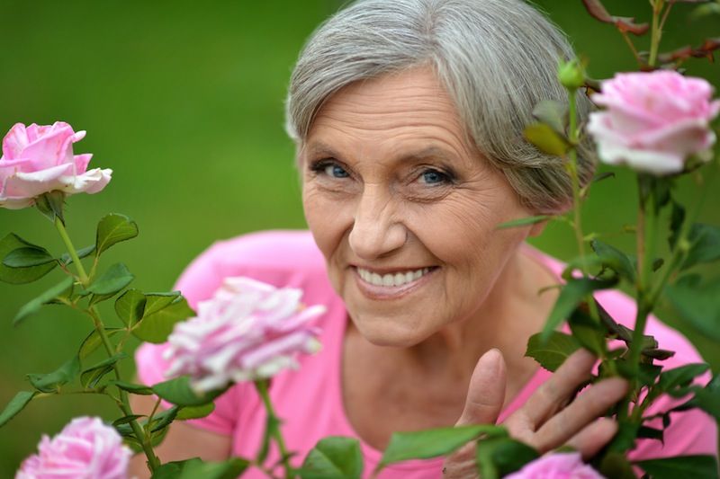 An older woman stands amid a bunch of flowers.