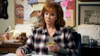 Bobbie at her desk holding a glass of wine in Happy&#039;s Place