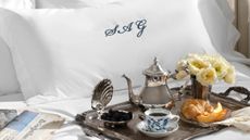 Swanky bedscape featuring a monogramed pillow sham and an ornate silver tray scattered with vintage-inspired silver serveware.