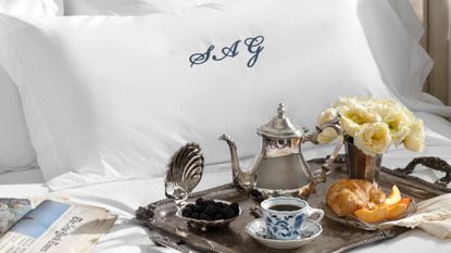 Swanky bedscape featuring a monogramed pillow sham and an ornate silver tray scattered with vintage-inspired silver serveware.