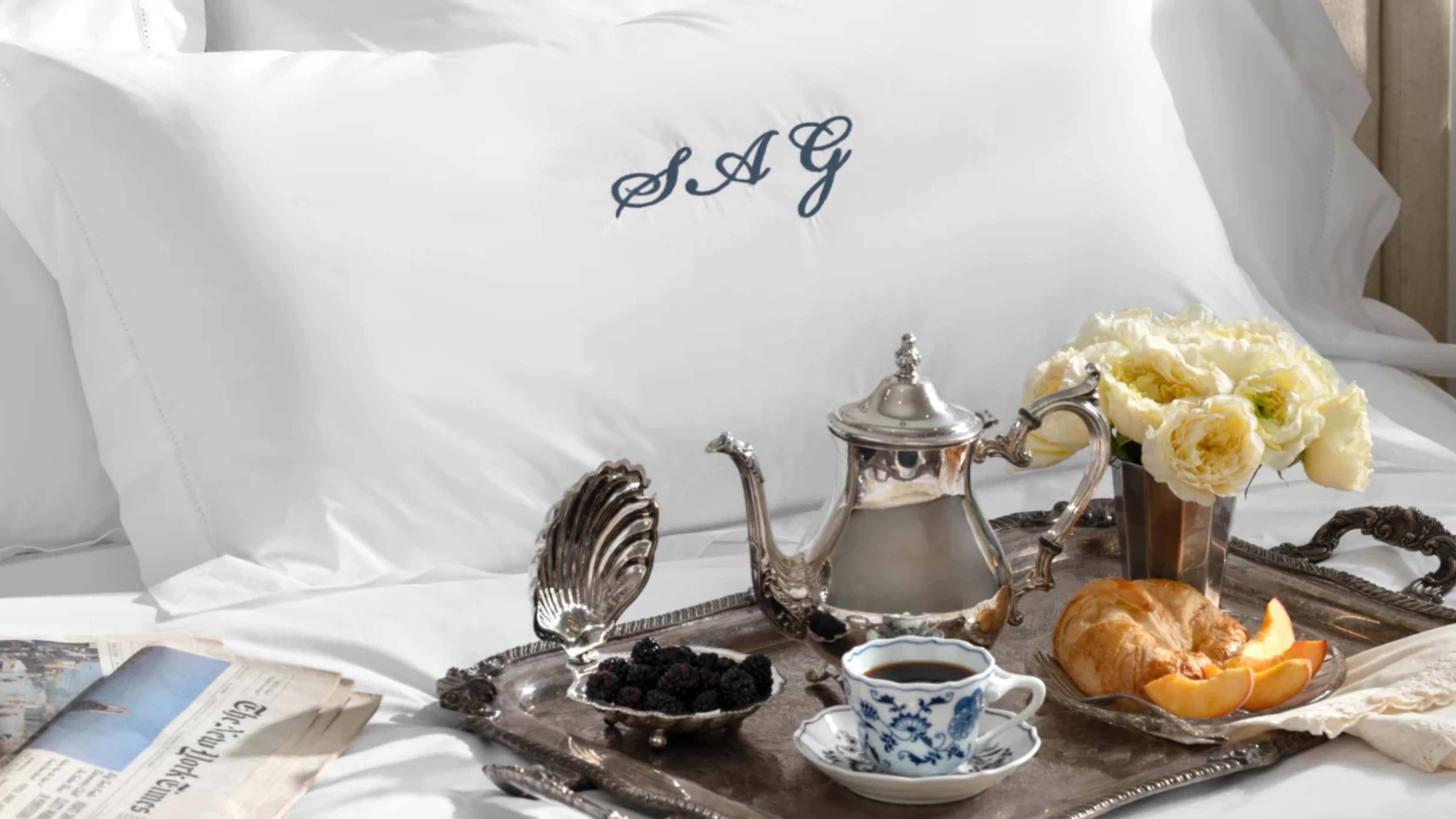 Swanky bedscape featuring a monogramed pillow sham and an ornate silver tray scattered with vintage-inspired silver serveware.