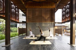 Three women practice yoga in a large covered outdoor space at Aleenta in Chiang Mai, Thailand